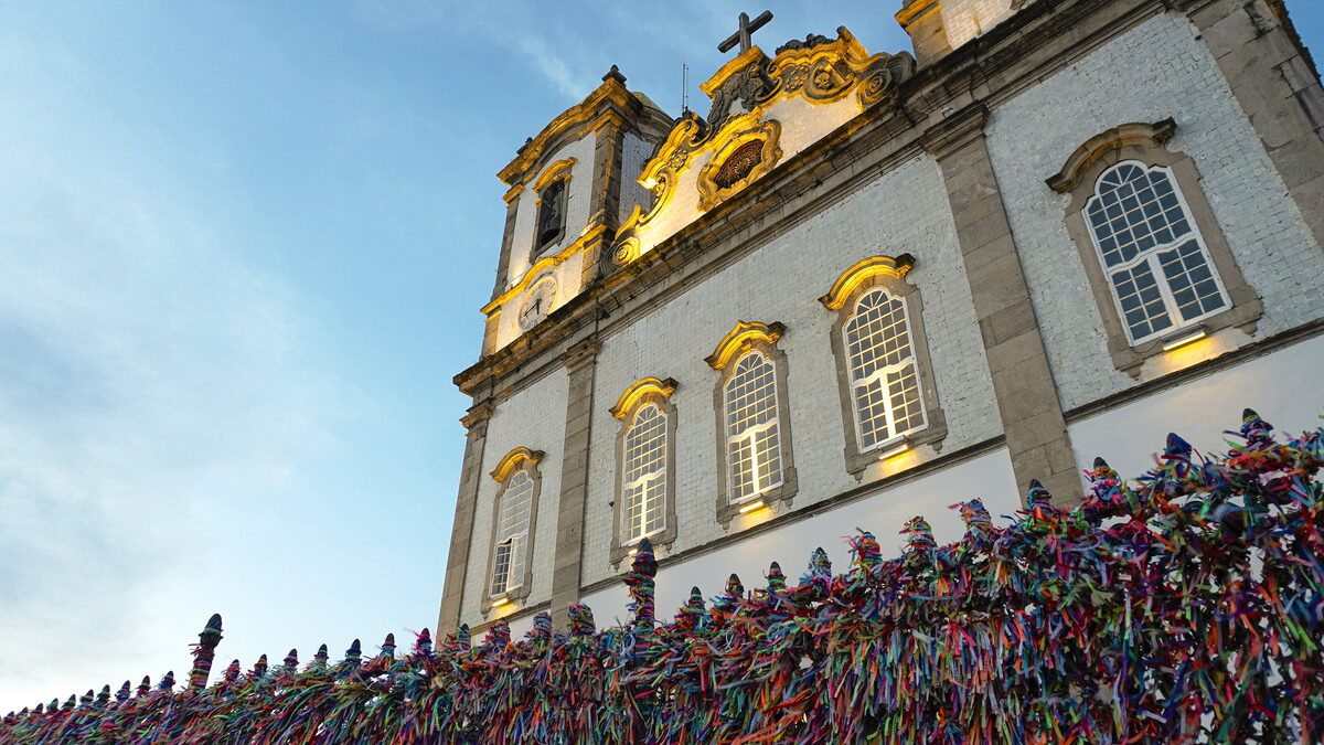 The white facade of the Senhor do Bonfim church, with its railings covered in colored ribbons