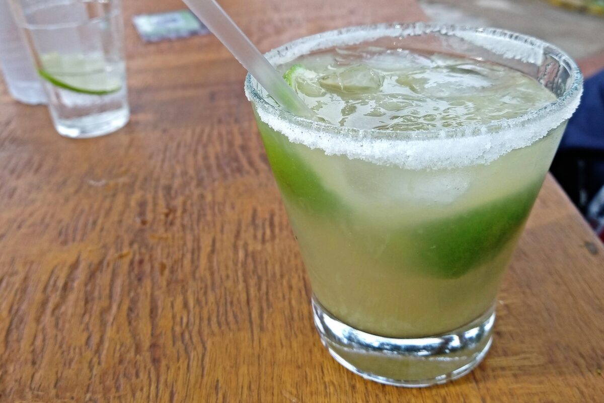 A caipirinha in a short glass with a sugared rim, lime and ice, on a wooden table
