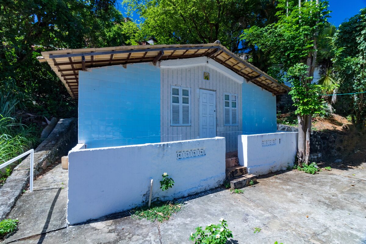 A small blue-tiled house with white shutters and a low white wall among trees, in the grounds of the Casa Branca terreiro