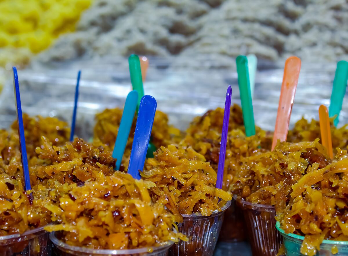 Cups of brown burnt-coconut cocada with colorful plastic spoons on a sweets stall