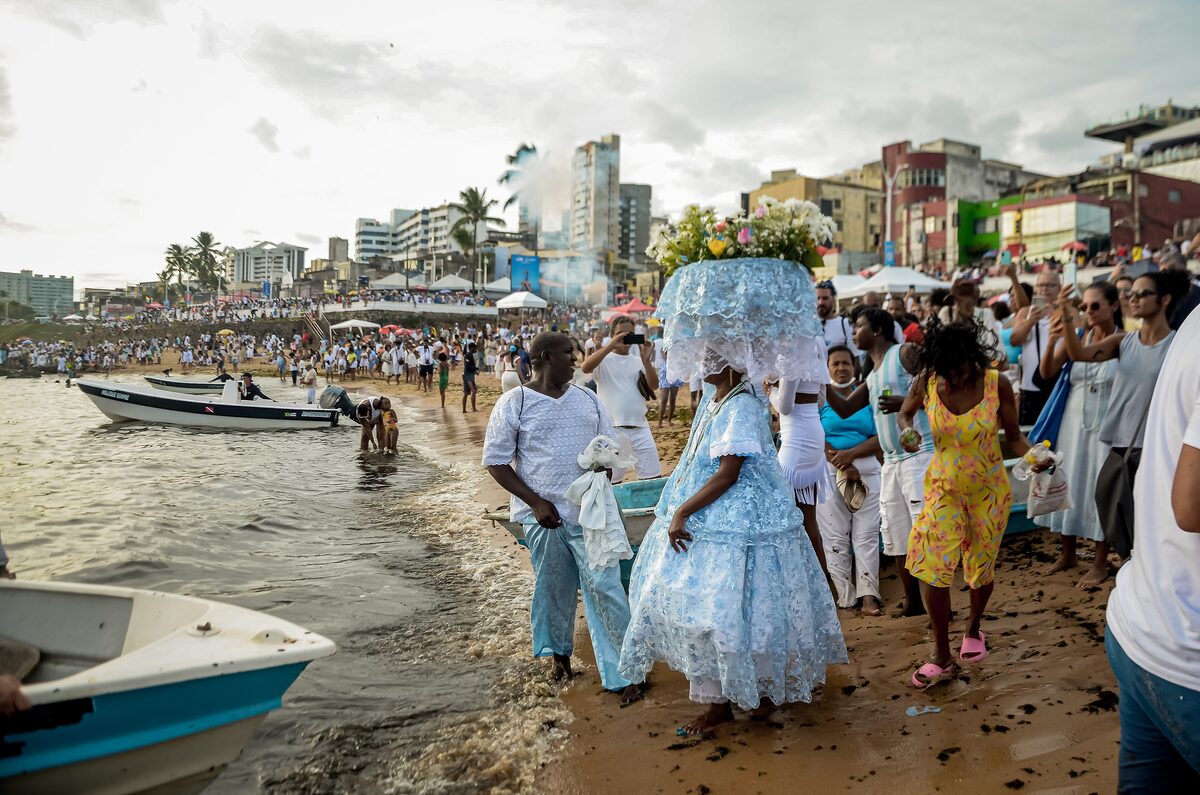 Devotees in white on the Rio Vermelho shore during the Iemanjá festival, with a decorated offering carried through the crowd