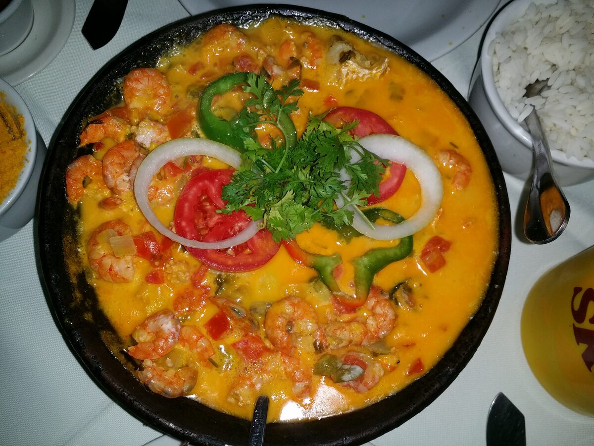 A shrimp moqueca in a pan, with tomato and pepper rings, onion and parsley on the orange stew