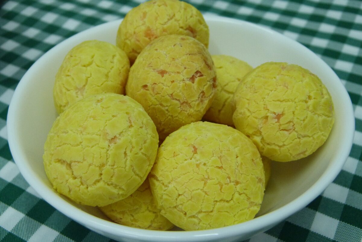 A white bowl of golden pão de queijo cheese bread balls on a green checked cloth