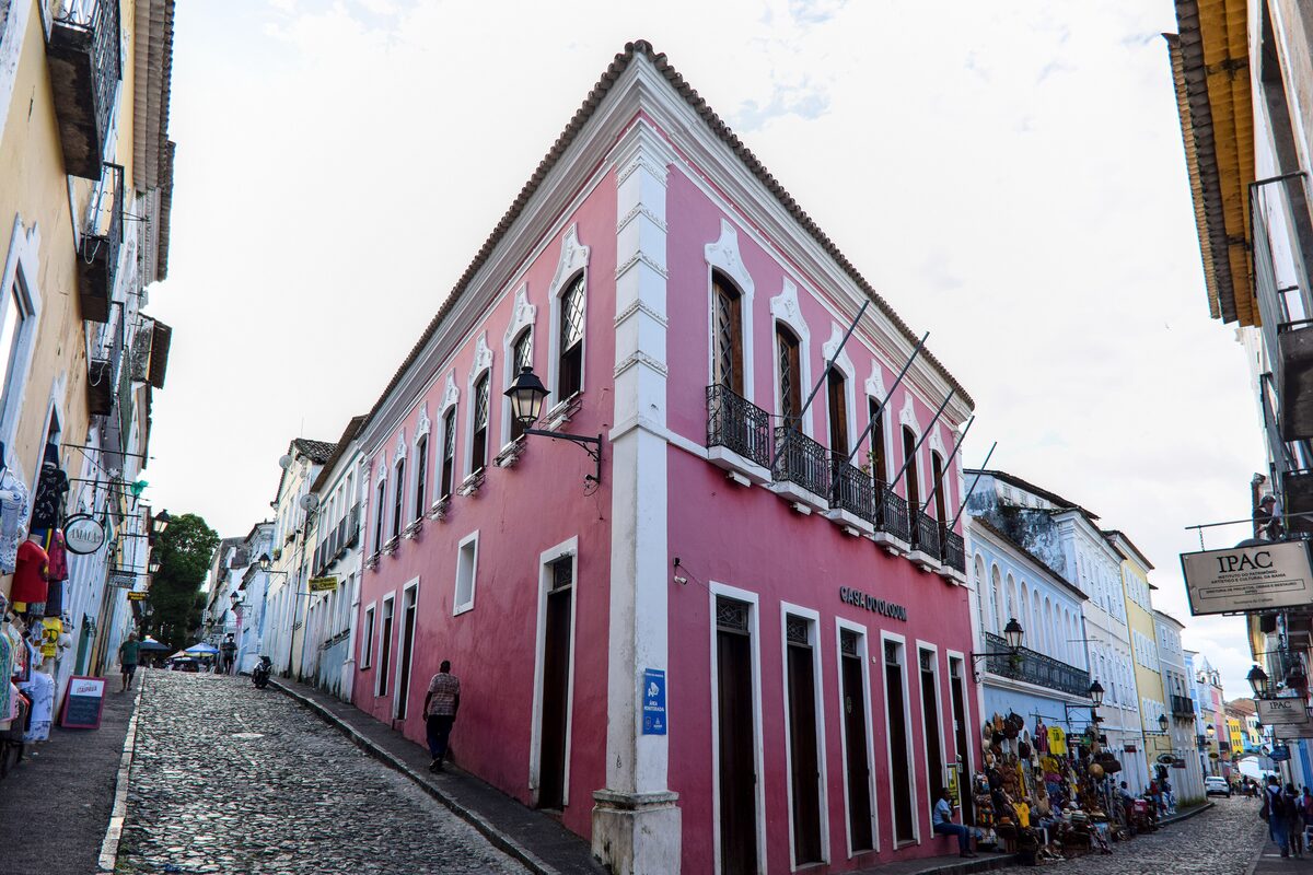 A pink colonial corner house on a steep cobbled lane in Pelourinho, with colorful facades along the street