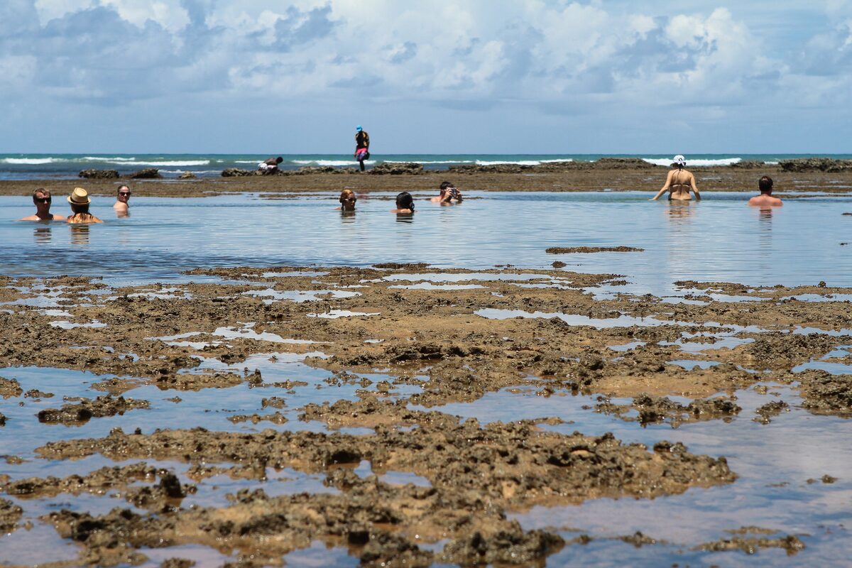 Natural tidal pools among the reef rocks at Praia do Forte, with bathers sitting in the shallow water