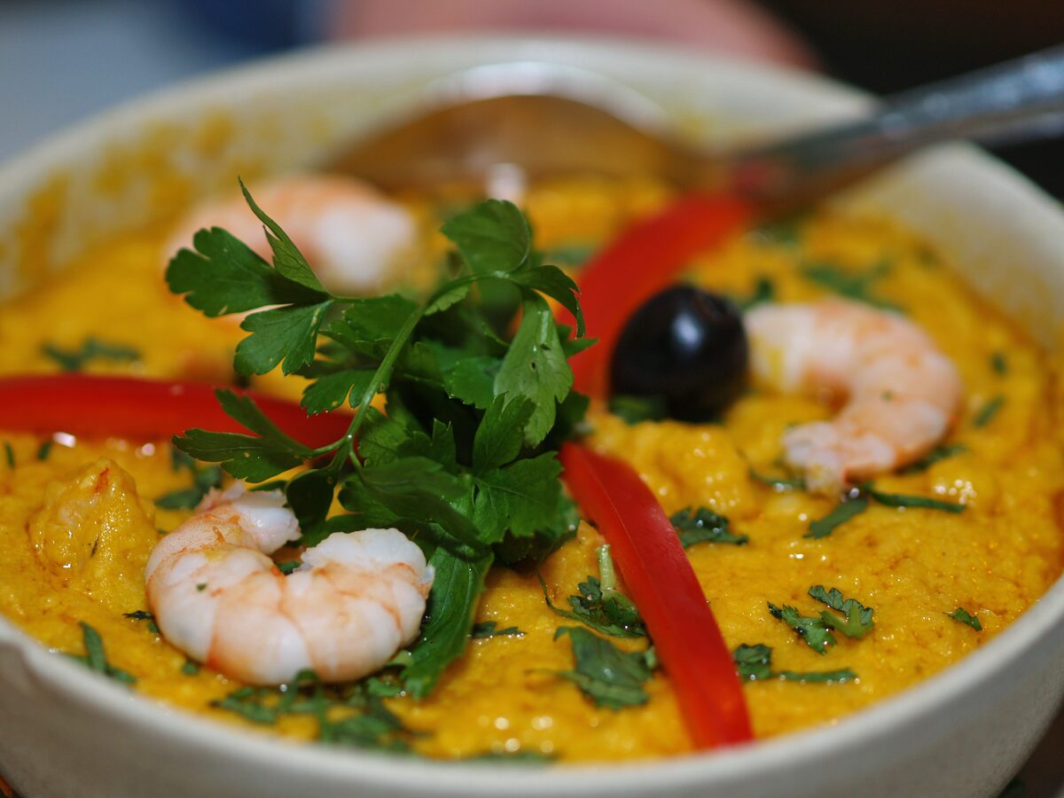 A bowl of vatapá, a creamy yellow shrimp paste garnished with parsley and red pepper