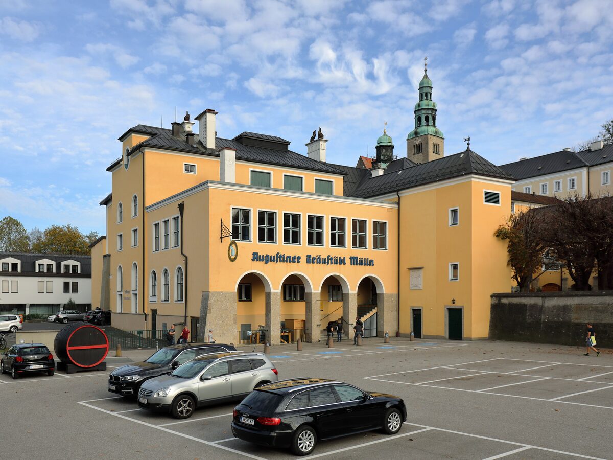 The yellow building of the Augustiner Bräu beer hall in Mülln, with its church tower behind