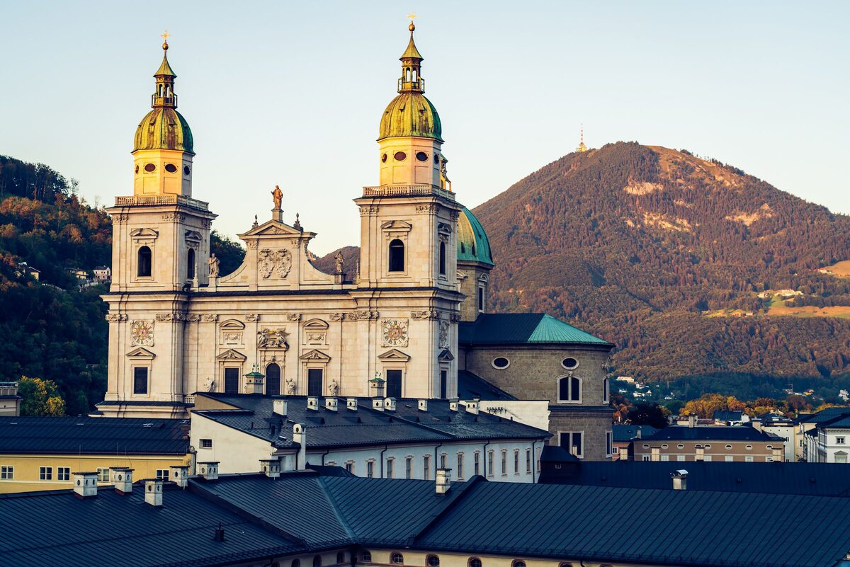 The twin towers and dome of Salzburg Cathedral above the old town roofs, with the wooded Gaisberg behind