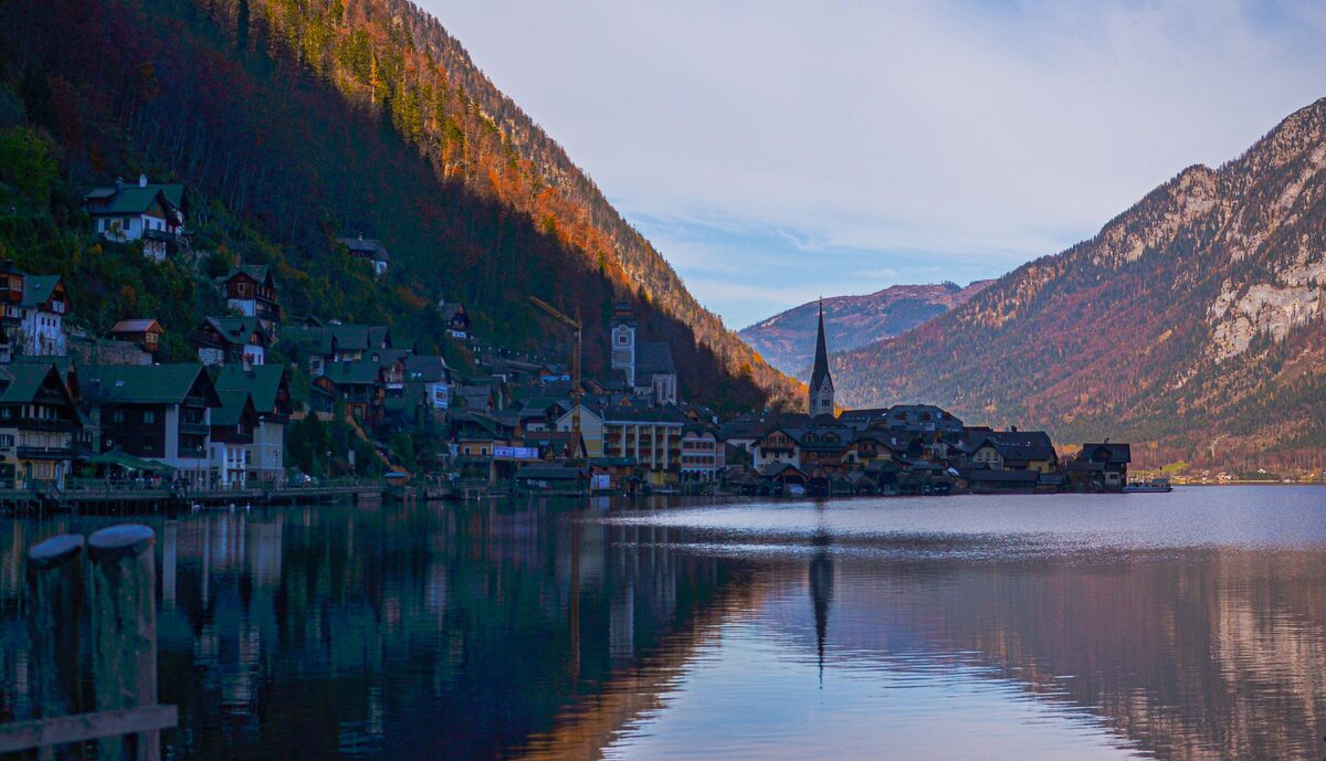 Hallstatt's houses and church spire reflected in the still lake under steep autumn mountains