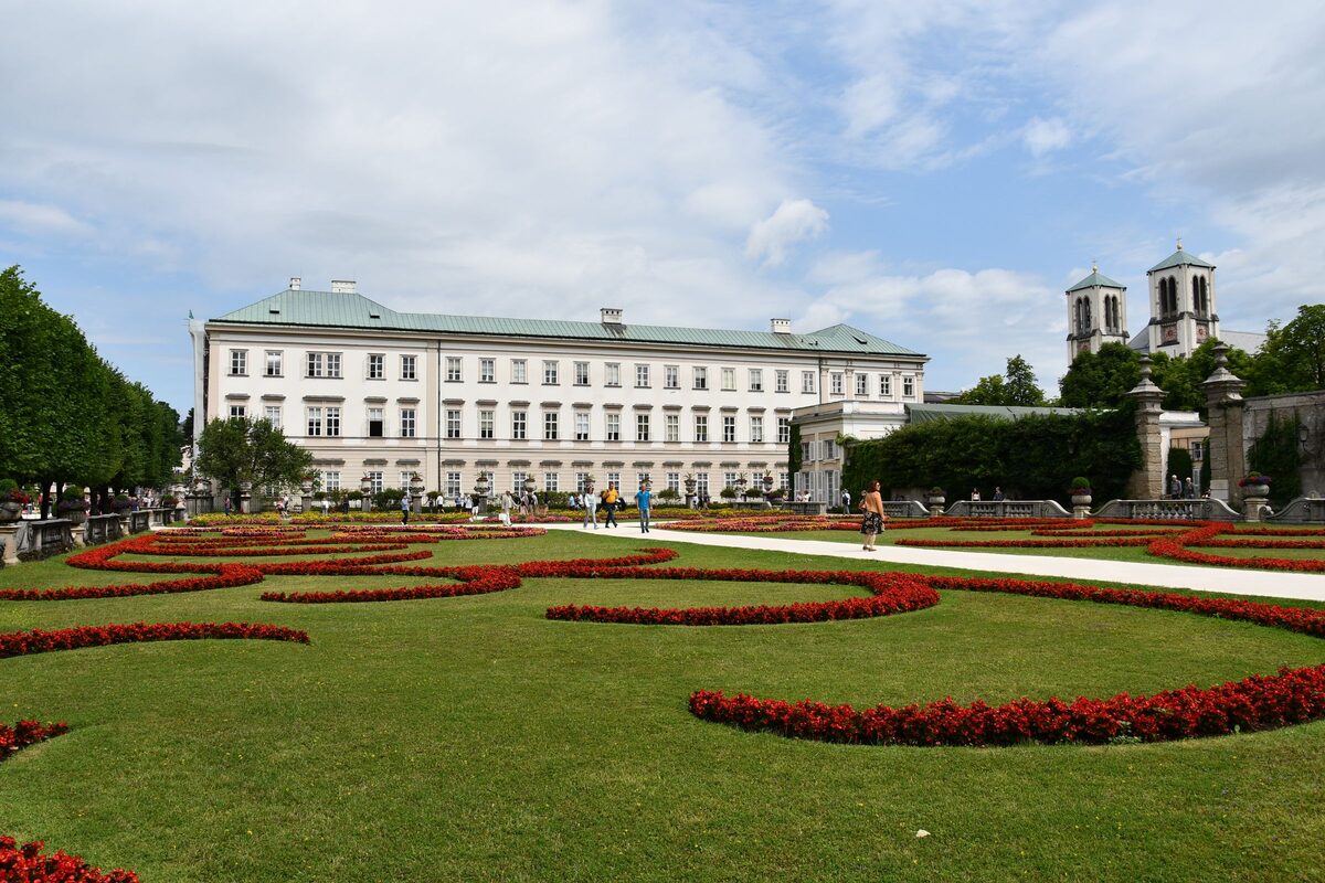 The red flower beds and lawns of the Mirabell Gardens in front of the long white Mirabell Palace