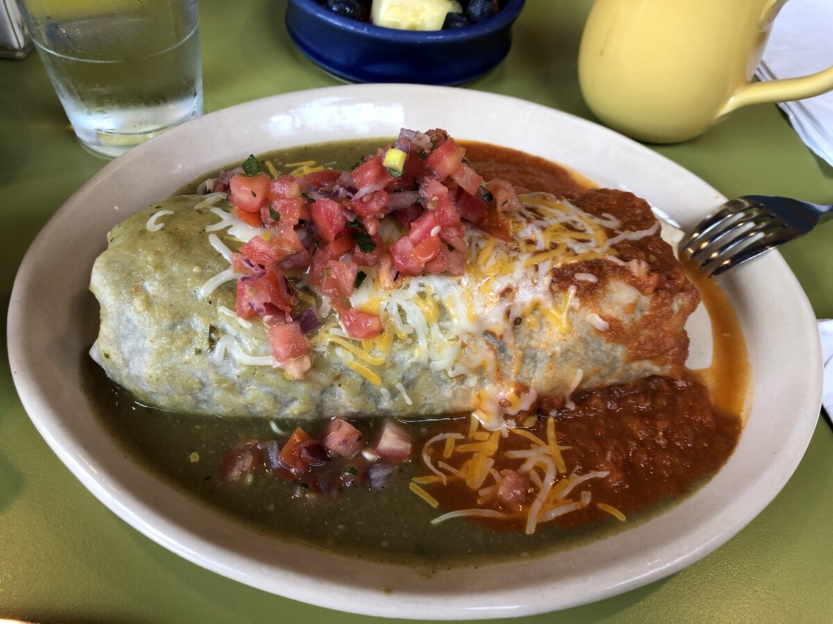 A smothered breakfast burrito with salsa, cheese and fresh tomato