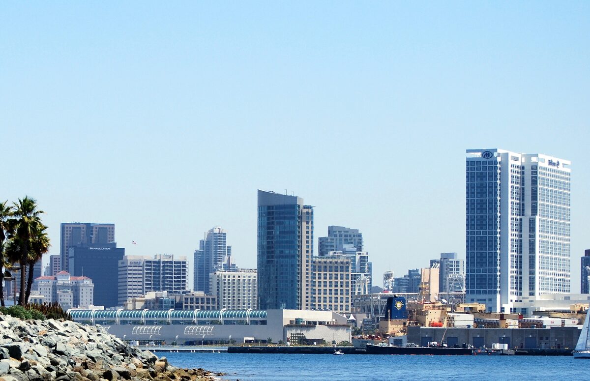 Downtown San Diego towers rising behind the bay and a rocky shore