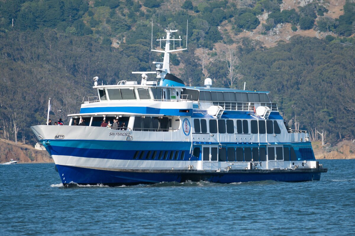 A blue-and-white Golden Gate Ferry crossing the bay with the Marin hills behind it