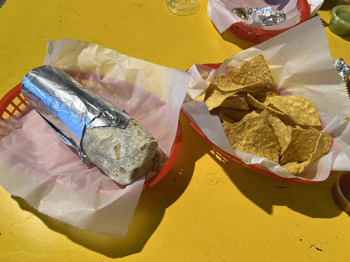 A foil-wrapped Mission burrito on paper next to a basket of tortilla chips