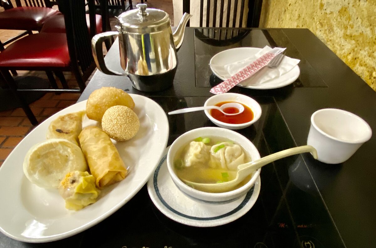 A plate of dim sum buns, dumplings and a spring roll with a bowl of wonton soup and a teapot in a Chinatown restaurant