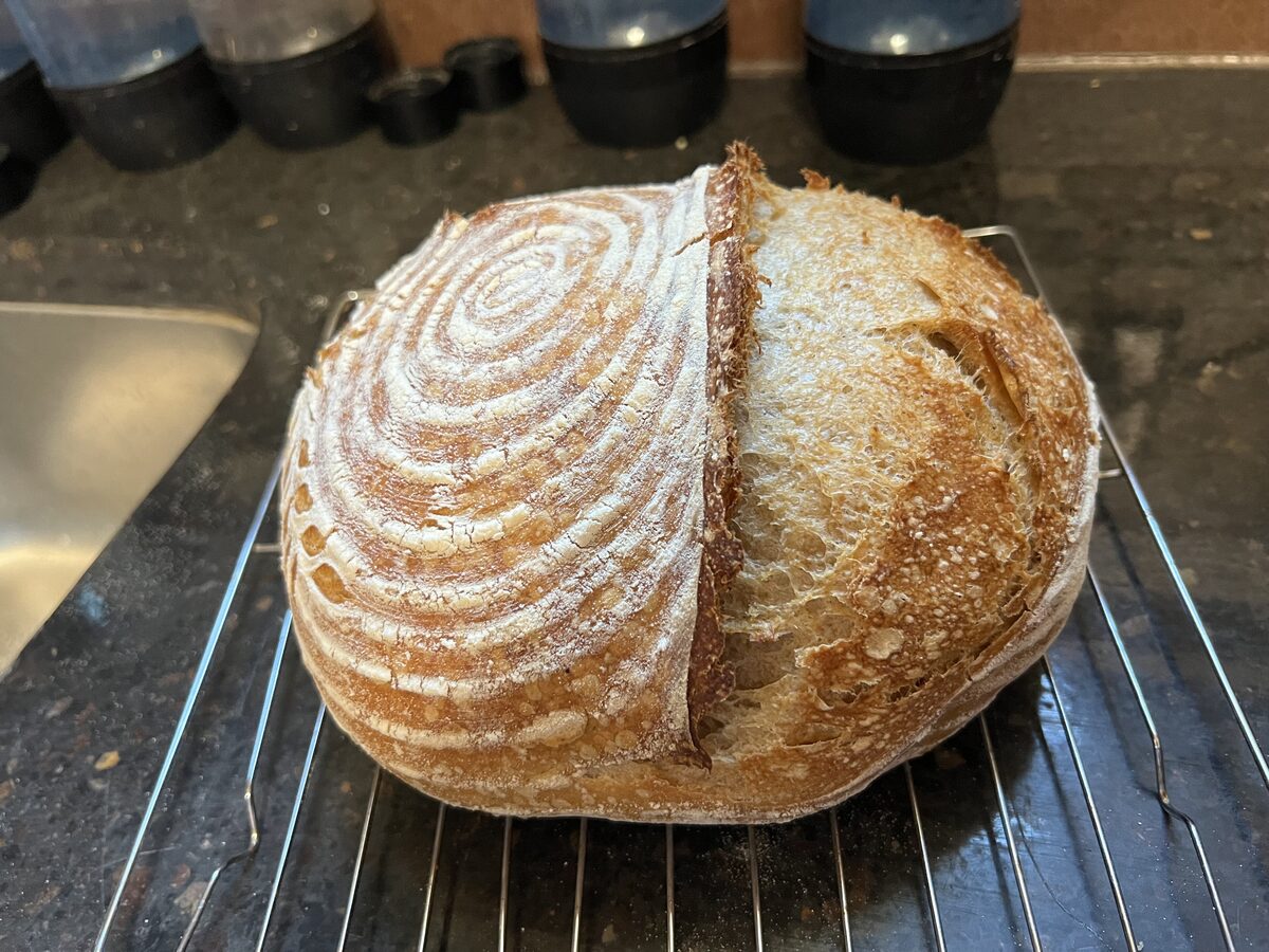 A round sourdough loaf with a floured spiral pattern and a single slash, cooling on a wire rack