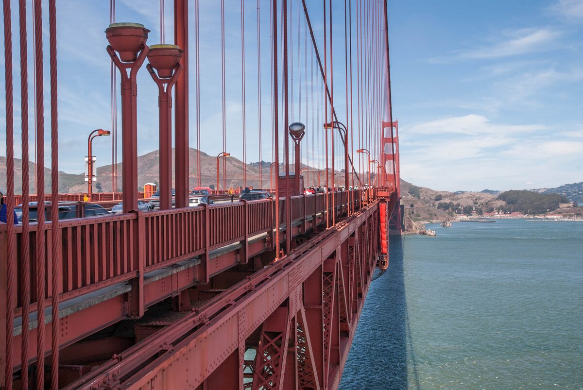 The Golden Gate Bridge seen from the sidewalk, with red railings, lamp posts and the Marin Headlands ahead