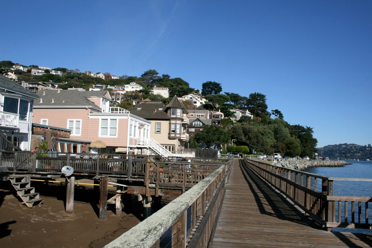 A wooden pier on the Sausalito waterfront with pastel houses climbing the hill behind it