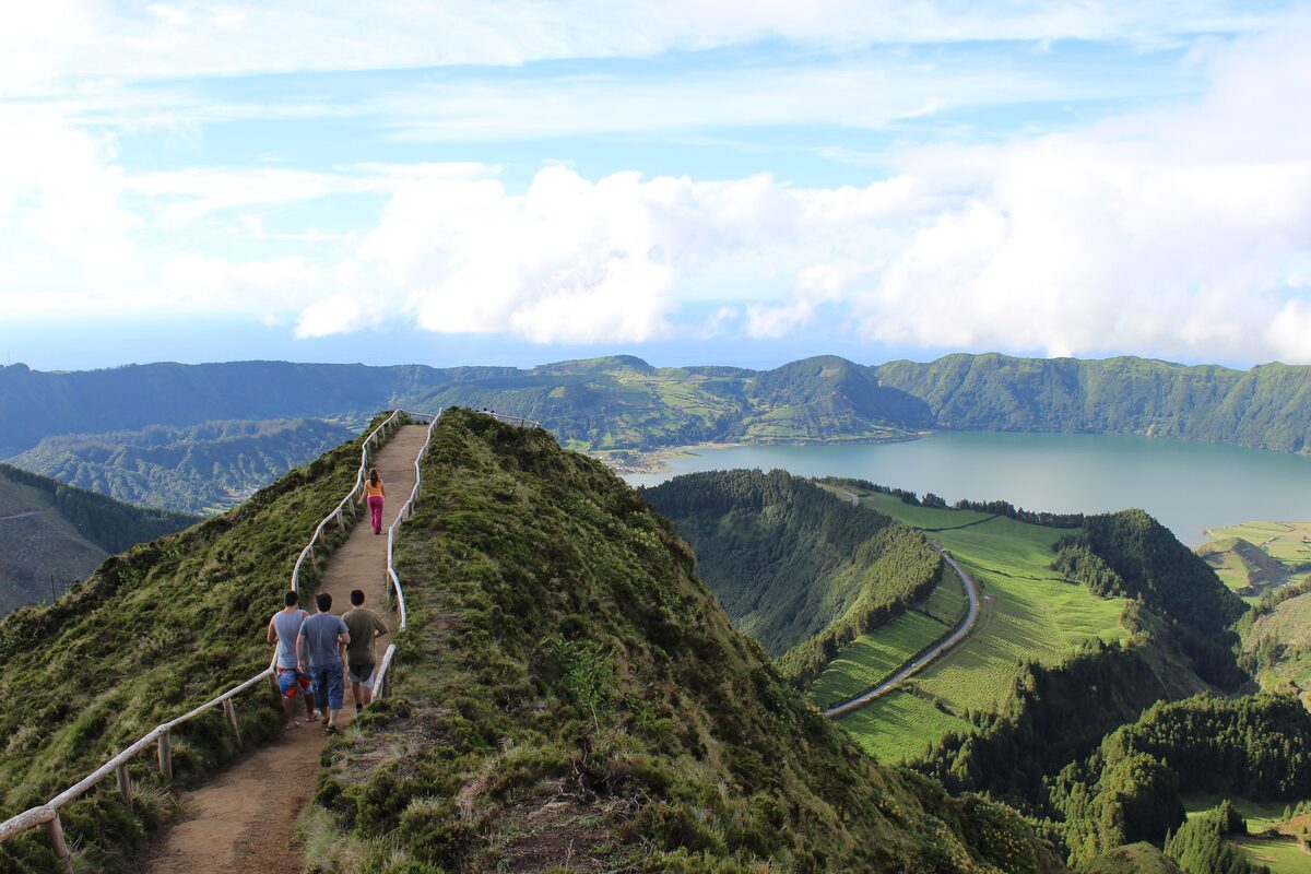 A wooden-railed path along a green ridge at the Boca do Inferno viewpoint, with the crater lakes of Sete Cidades beyond
