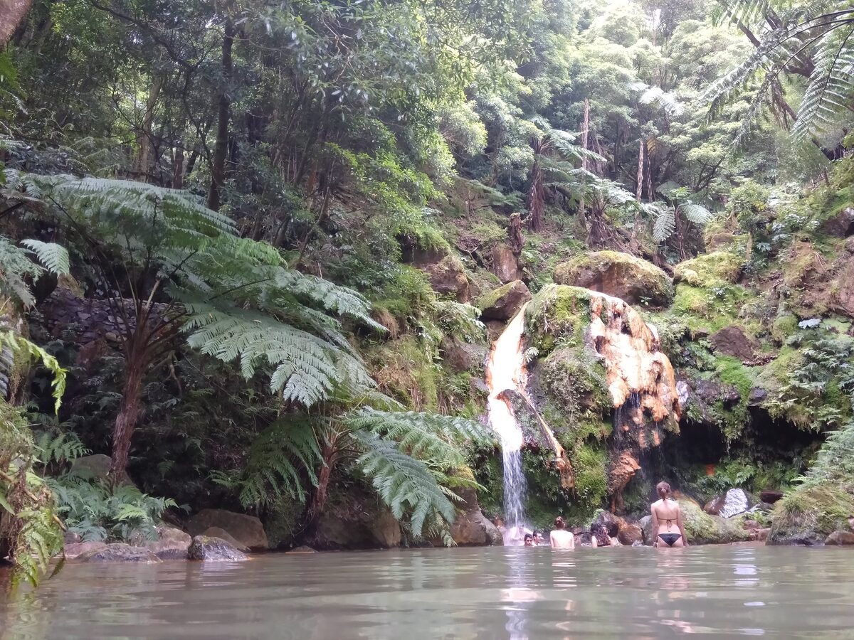 A warm waterfall pour into a pool in the fern-lined Caldeira Velha, with bathers in the water