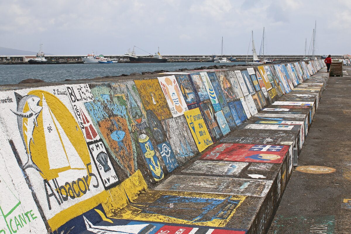 The breakwater of Horta harbour covered in painted murals of sailing boats and flags