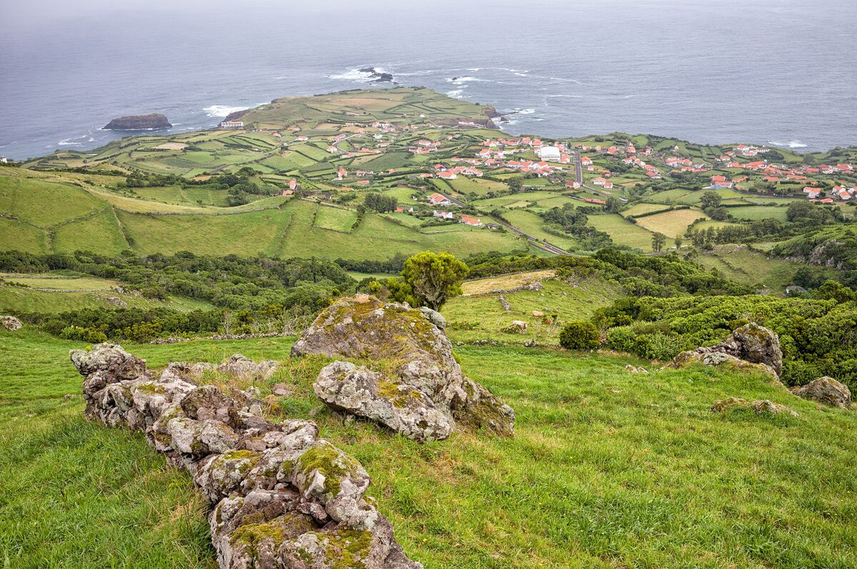 Green fields, stone walls and a red-roofed village on the coast of Flores