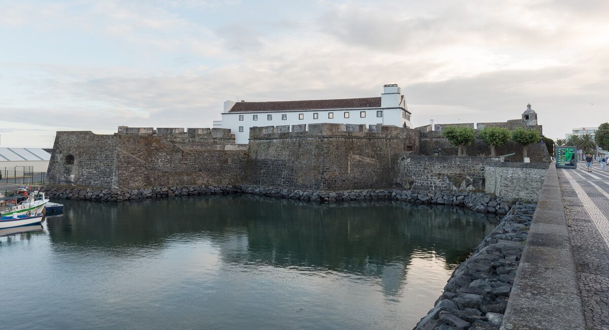 The stone walls of the São Brás fort rising from the water of the Ponta Delgada harbor, with the white fort buildings above