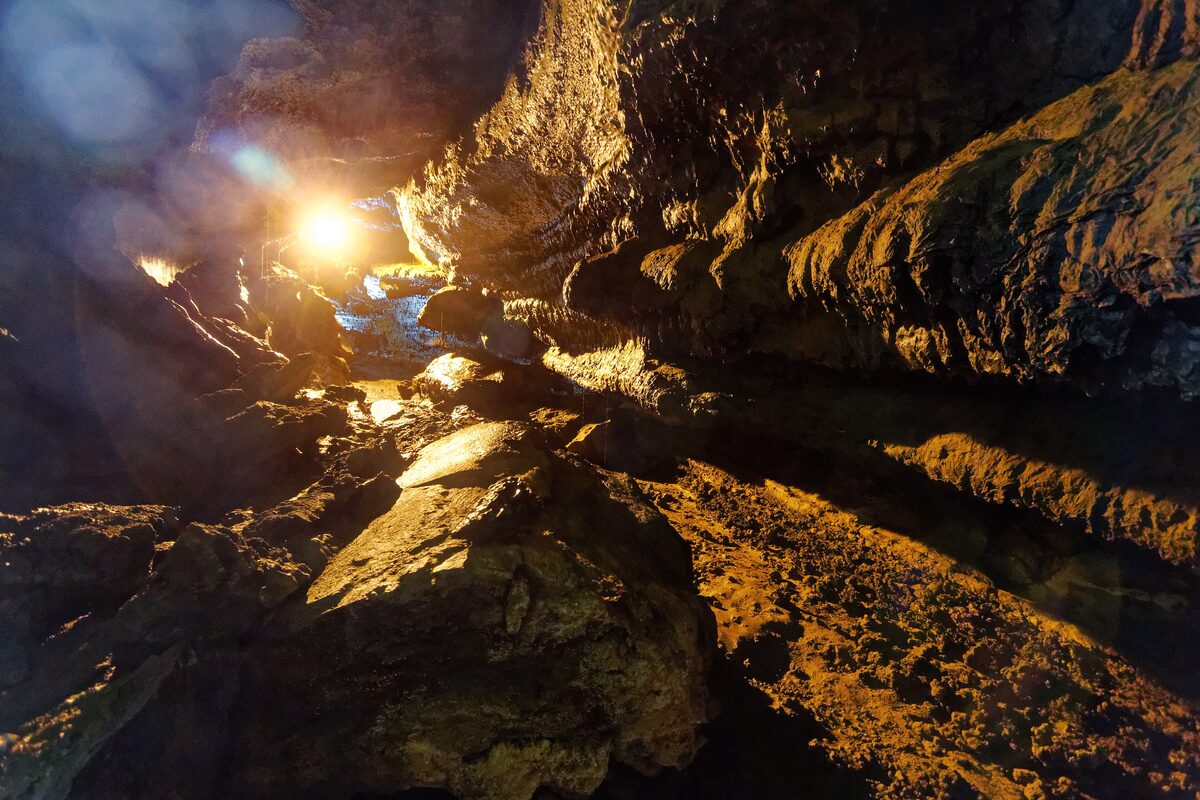 Light falls on the dark, ridged rock walls inside the Gruta do Carvão lava tube