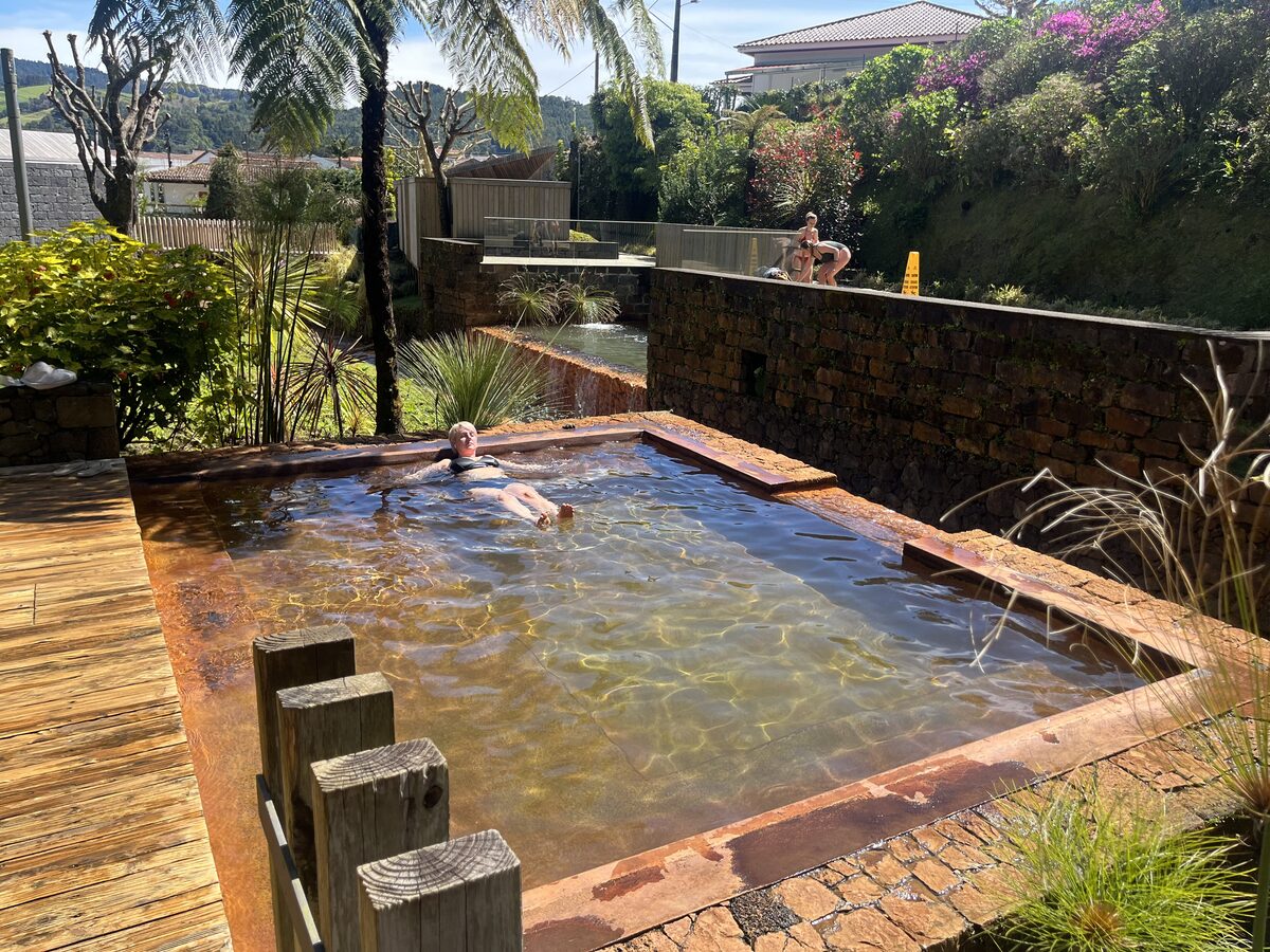 A rectangular hot pool with stone edges and a wooden deck at Poça da Dona Beija, with steam over the water