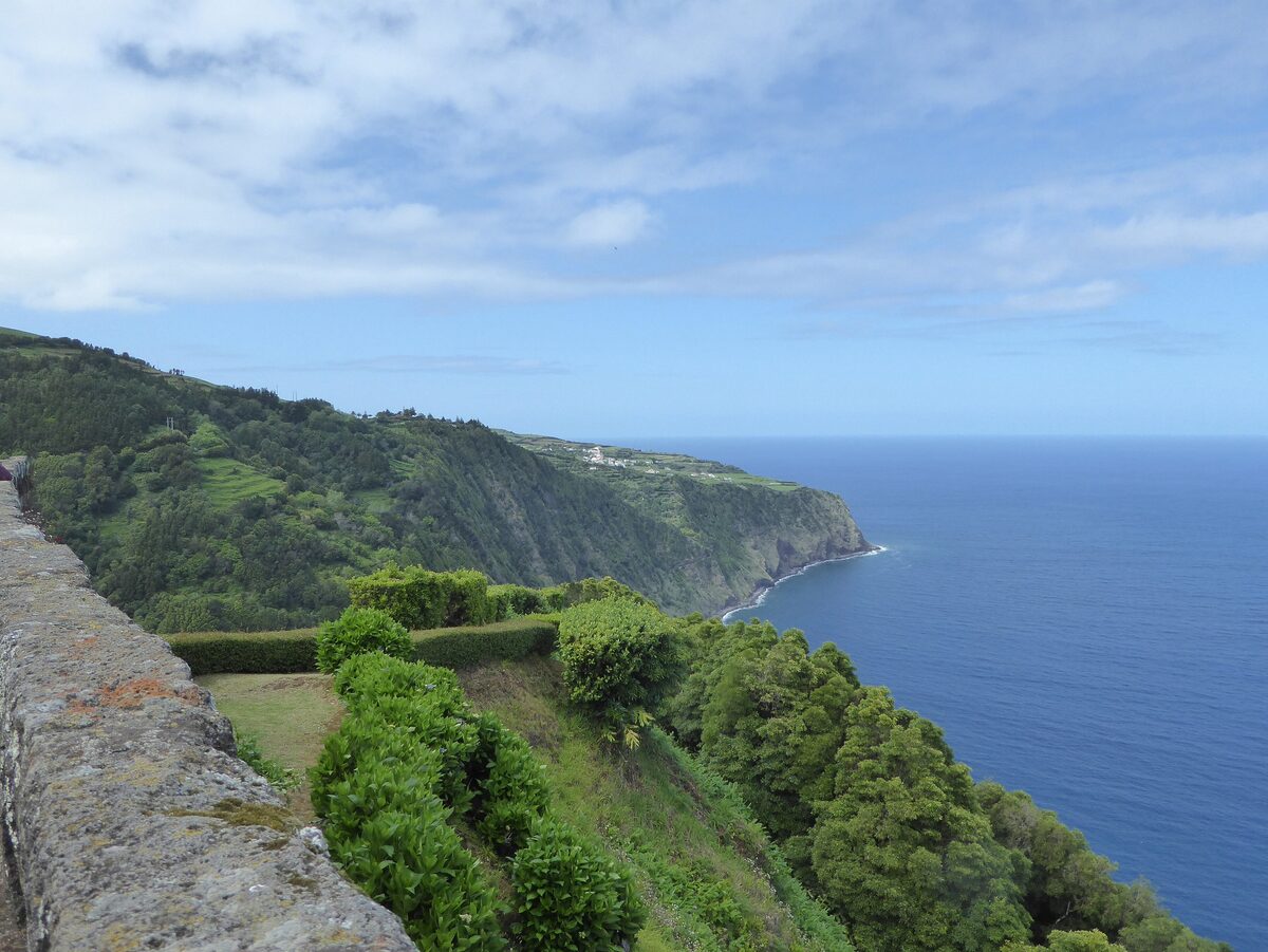 A stone wall and hedges at the Ponta da Madrugada viewpoint, with forested cliffs falling to the deep blue sea of the northeast coast