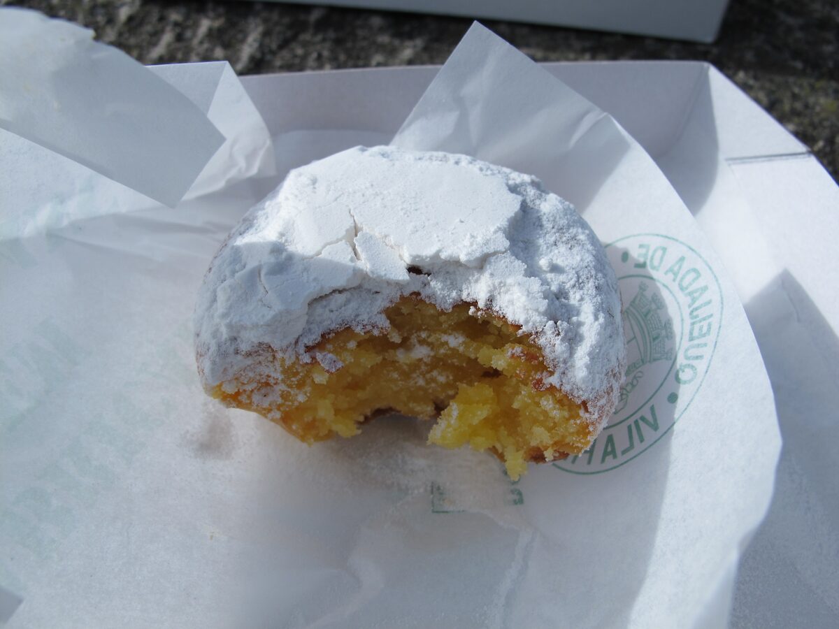 A queijada da Vila dusted with sugar, bitten open to show its yellow cheese-custard filling