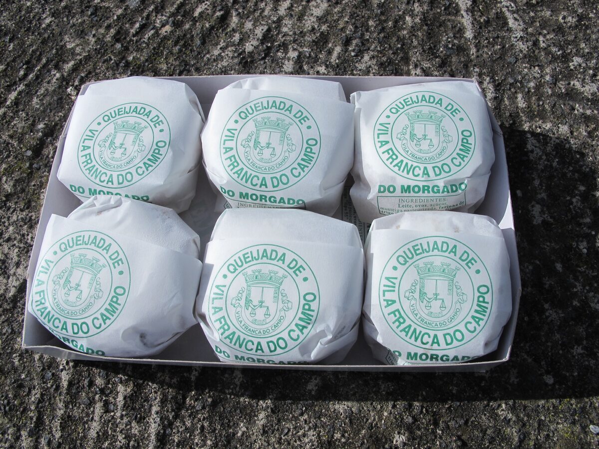 A box of six queijadas da Vila, each tart wrapped in white paper stamped with the Vila Franca do Campo crest