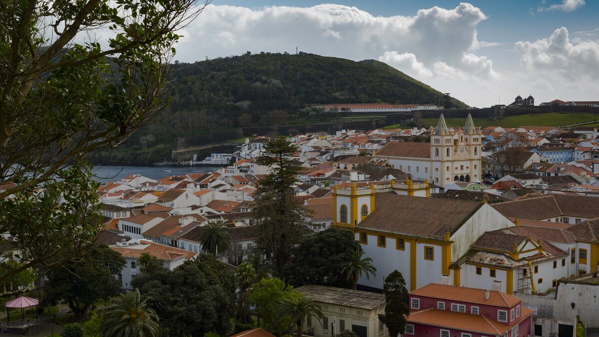 The white and yellow churches and red-tiled roofs of Angra do Heroísmo seen from above, with the green hill of Monte Brasil behind