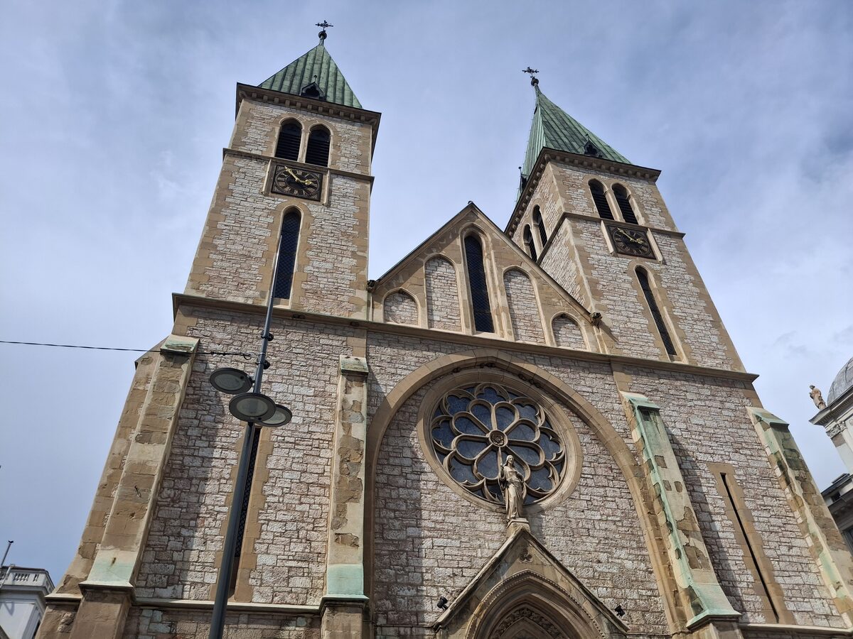 The twin towers and rose window of the Sacred Heart Cathedral, built of pale stone, seen from the street below