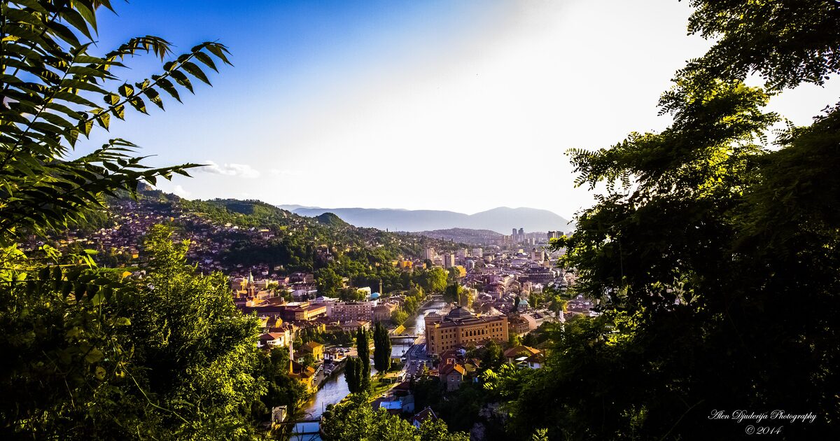 The old town of Sarajevo seen through trees, red roofs stepping down the Miljacka valley toward the hills