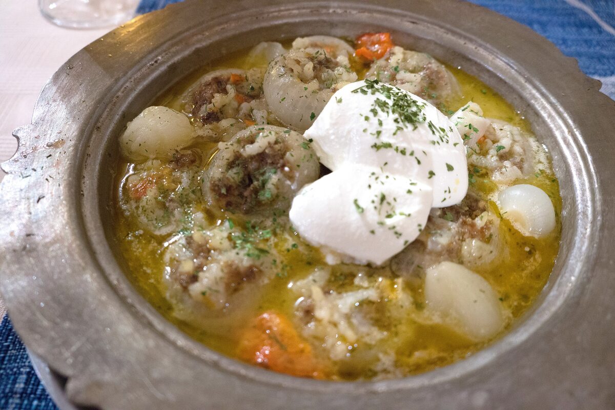 A pewter dish of sogan-dolma, small onions stuffed with rice and minced meat in broth, topped with a spoonful of yogurt