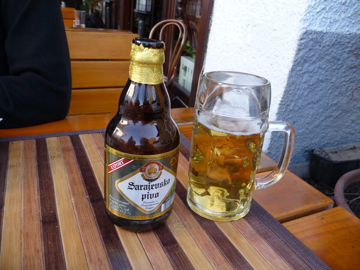 A bottle of Sarajevsko Pivo beside a glass mug of lager on a wooden table