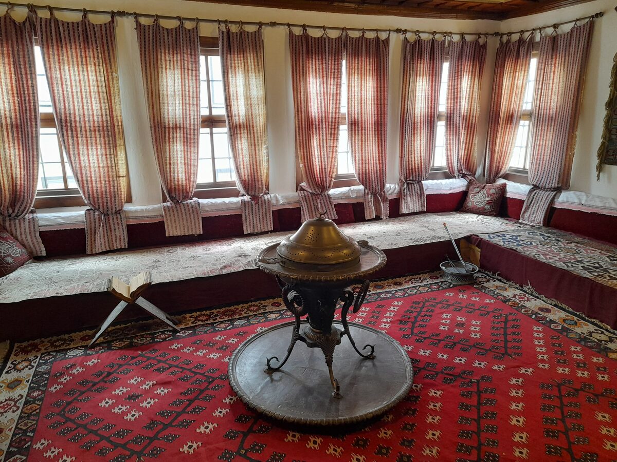 The selamlik room of Svrzo's House with a brass tray table on a red rug, cushioned divans and tall curtained windows