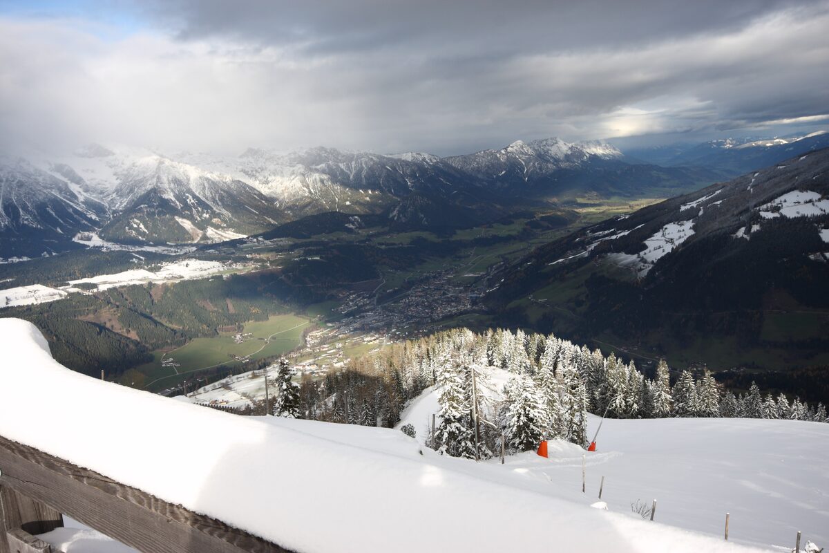 The view from the Hochwurzen summit down the Enns valley, with fresh snow on the railing and sun breaking through the clouds