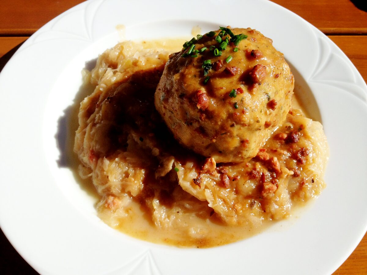 A bacon dumpling with gravy and chives on a bed of sauerkraut, on a white plate