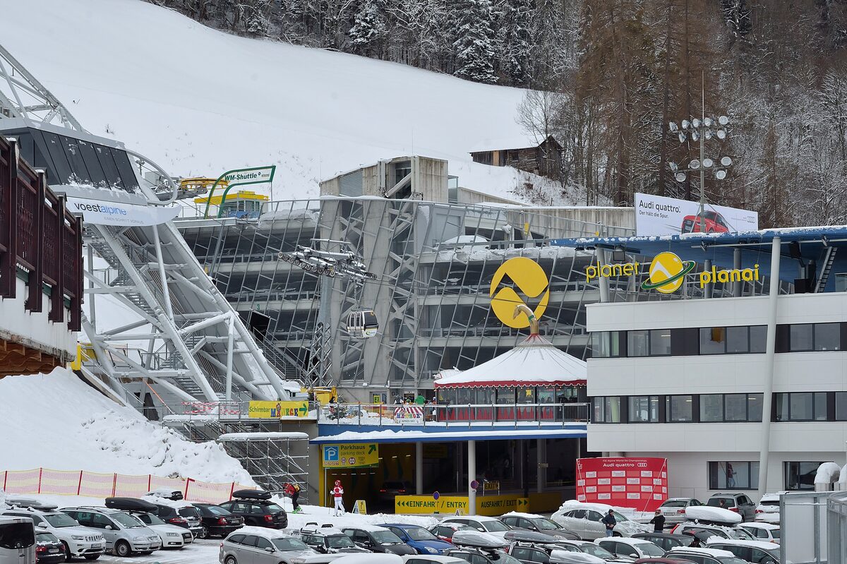 The Planai valley station in winter, with snow on the roof, a car park and the yellow Planai sign