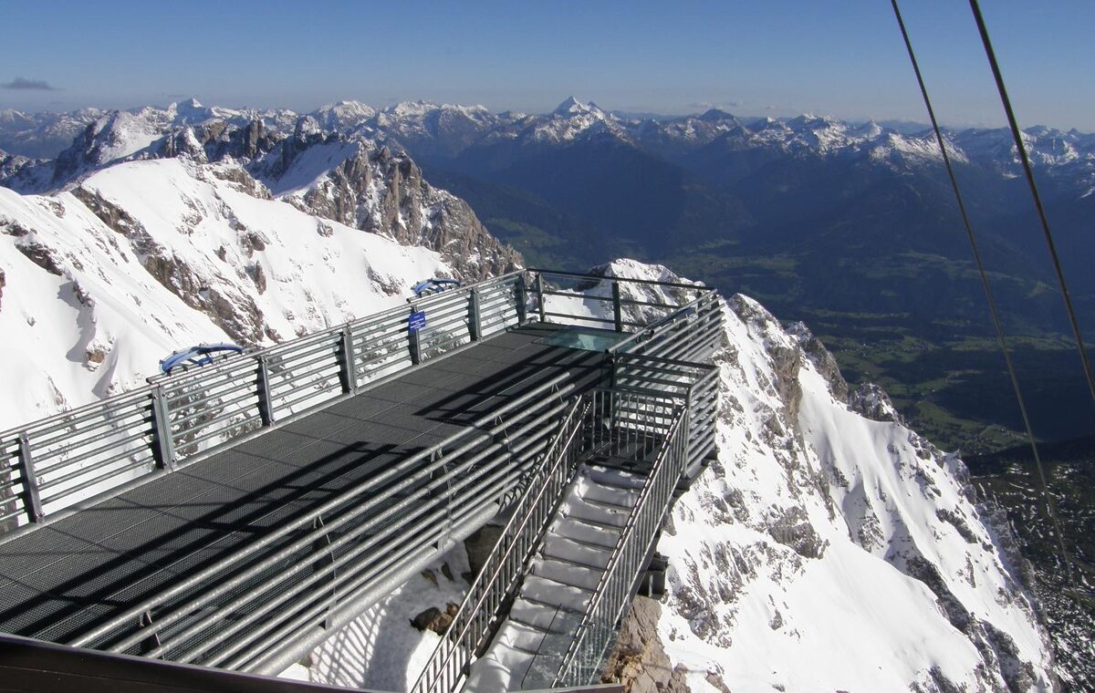 The Dachstein Skywalk, a steel viewing platform jutting out over a snowy rock face, with mountain ranges and the valley beyond