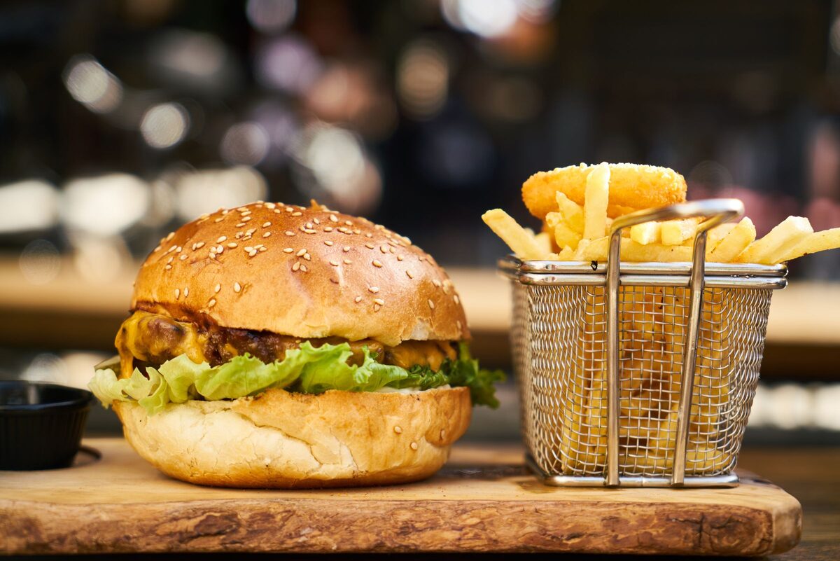 A burger on a wooden board with a basket of fries