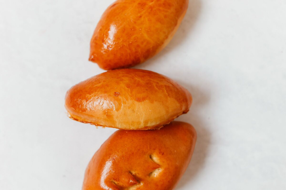 Three golden-brown baked piroshky on a white surface