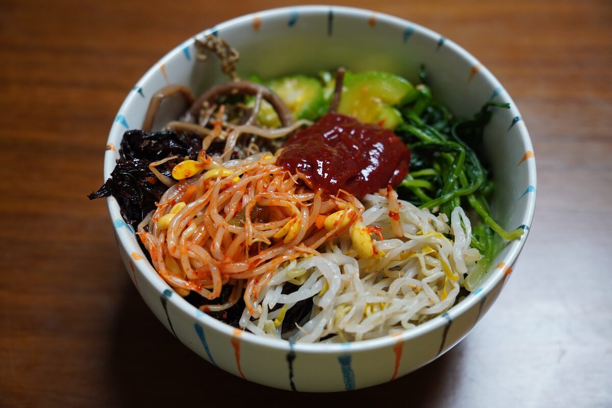 A bowl of bibimbap with seasoned vegetables, seaweed and a spoonful of red chili paste on top