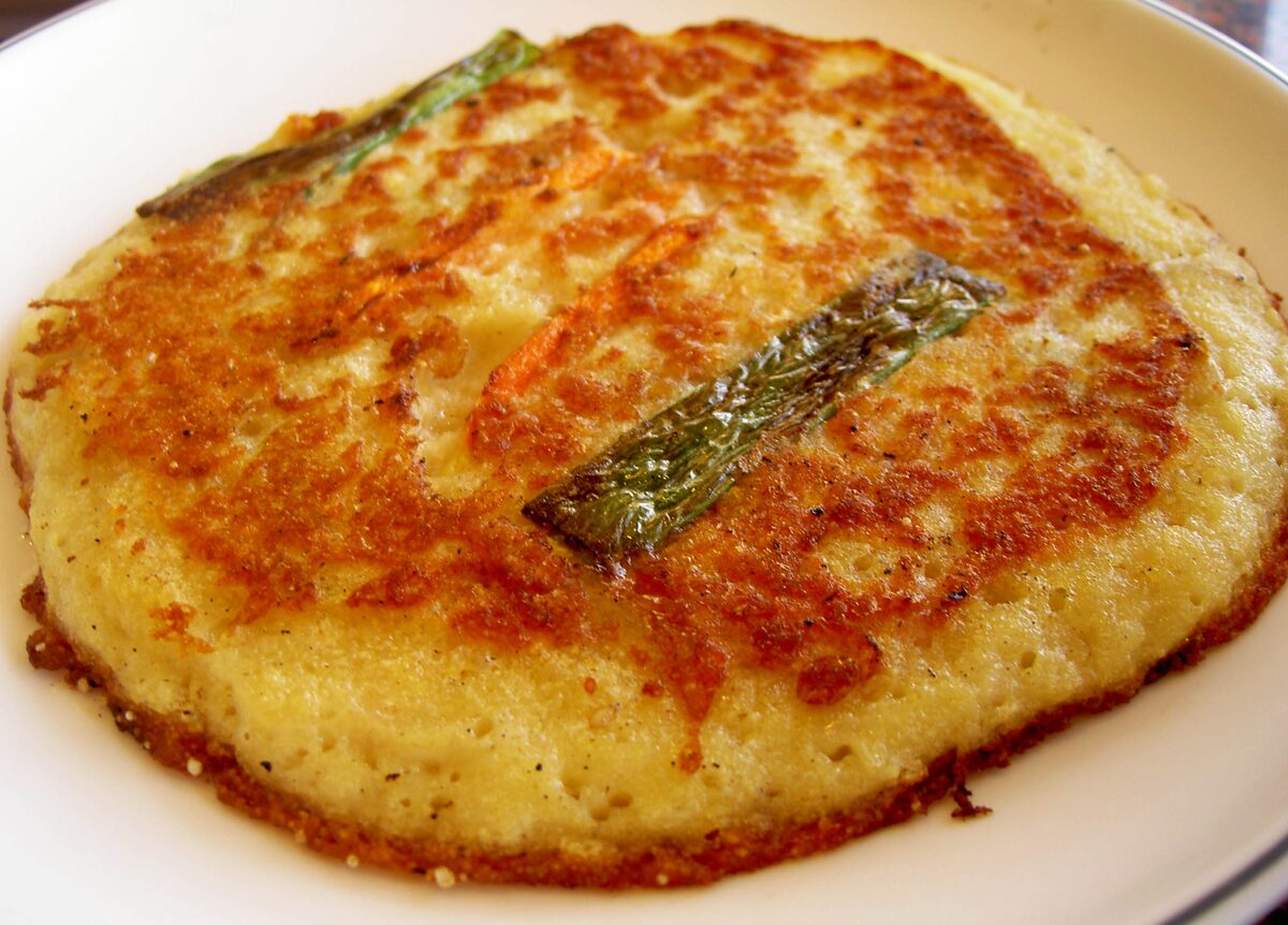 A thick golden bindaetteok mung bean pancake, crisp and browned, with a green chili strip on top