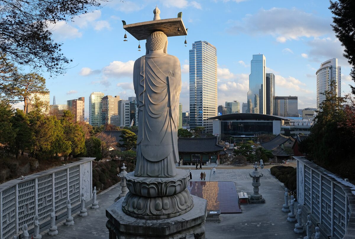 A stone statue of Maitreya Buddha at Bongeunsa with the Gangnam towers rising behind it