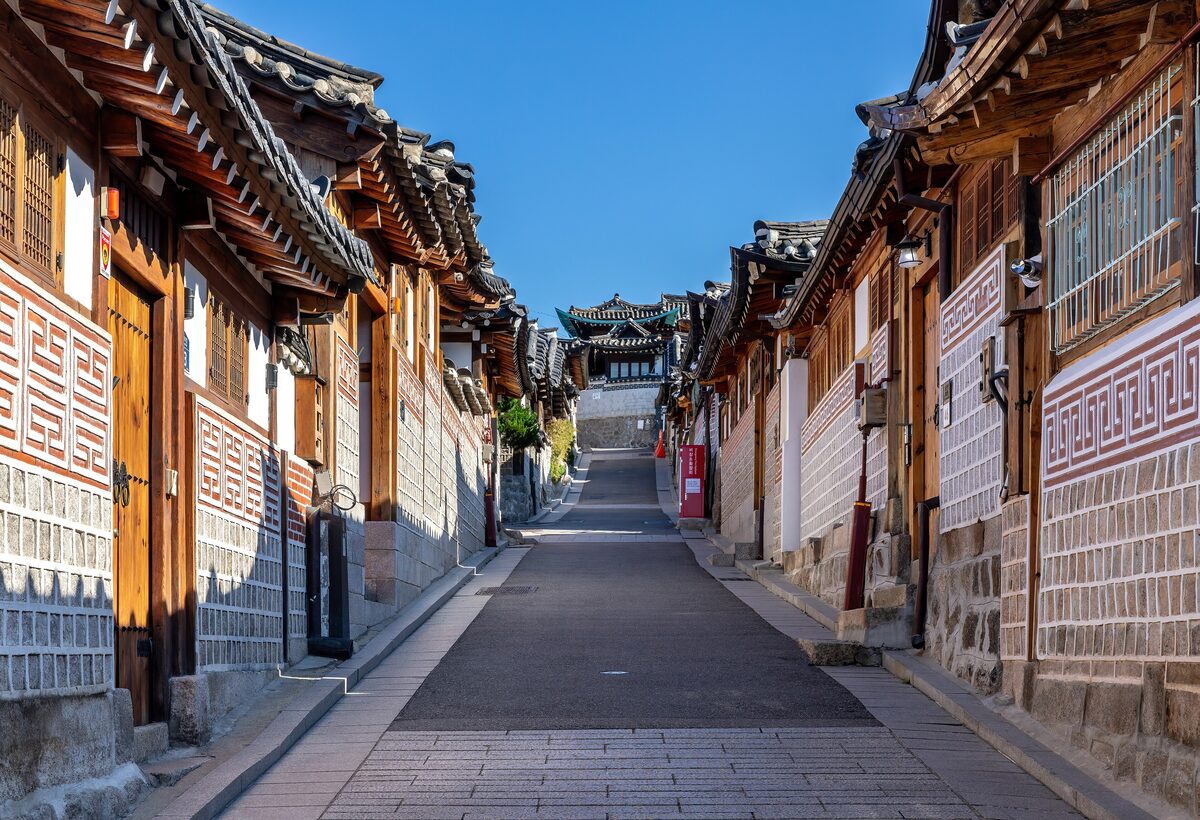 A narrow lane in Bukchon lined with tiled-roof hanok houses and wooden gates under a clear blue sky