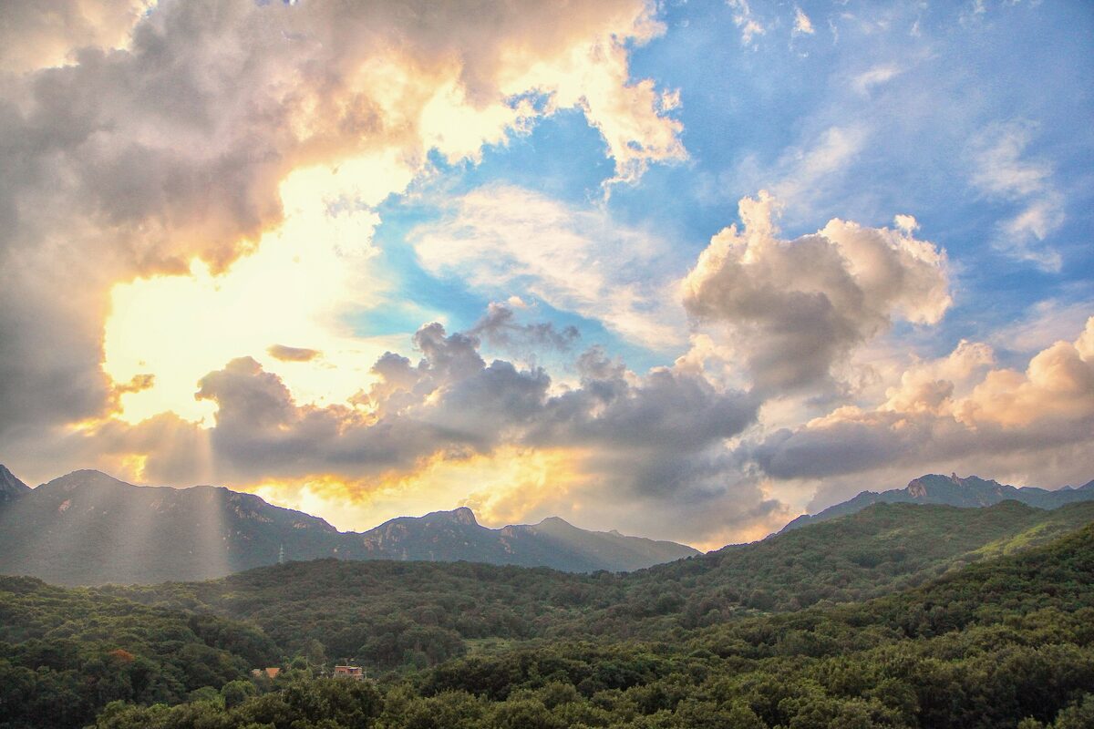 Sunlight breaking through clouds over green wooded ridges in Bukhansan National Park