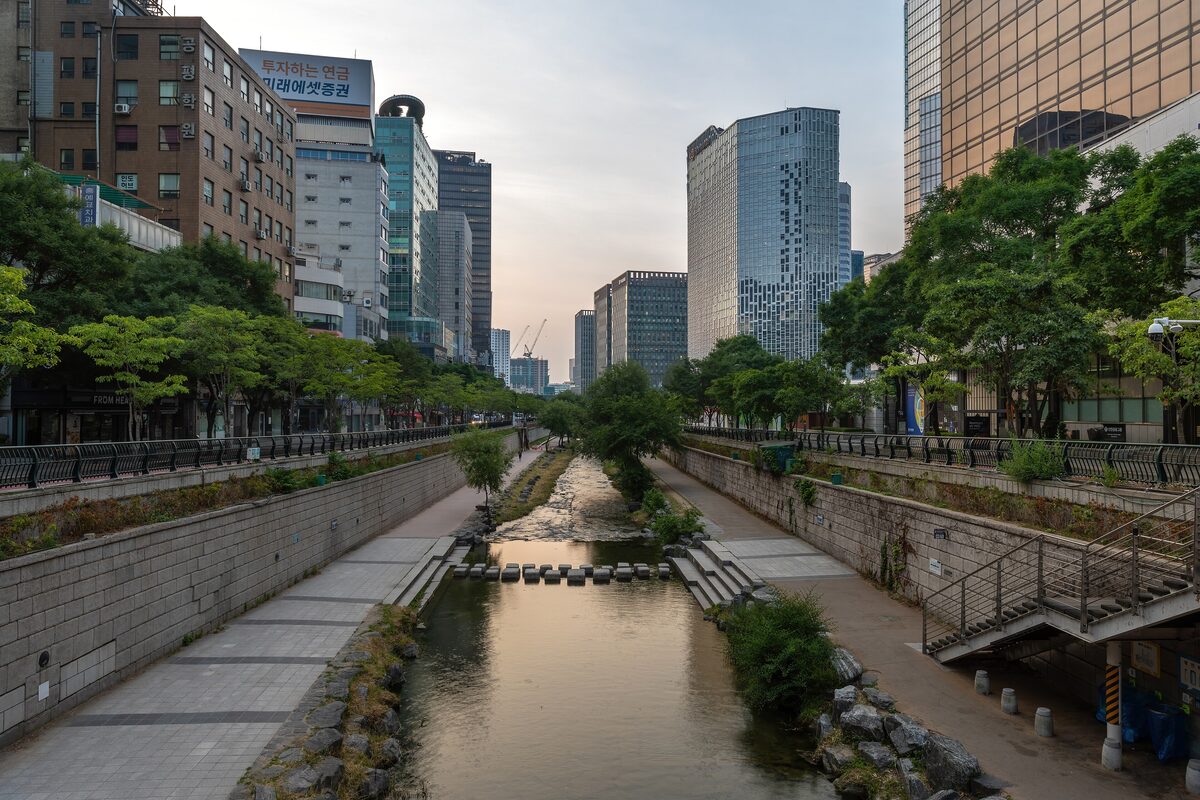 The Cheonggyecheon stream running between stone walkways and tree-lined streets, with office towers behind